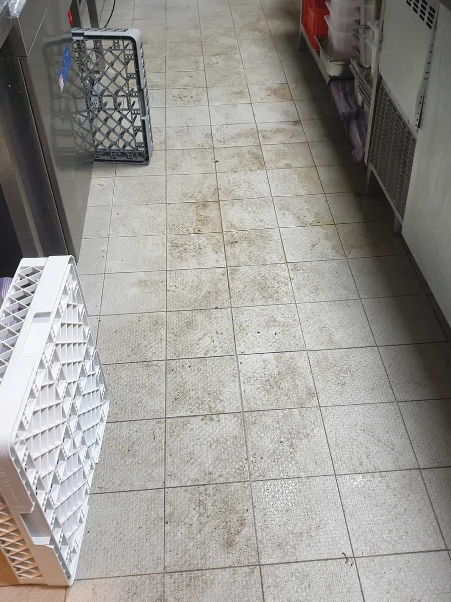 Gefliester Boden einer Küche mit dunklen Schmutzspuren, vor der Reinigung