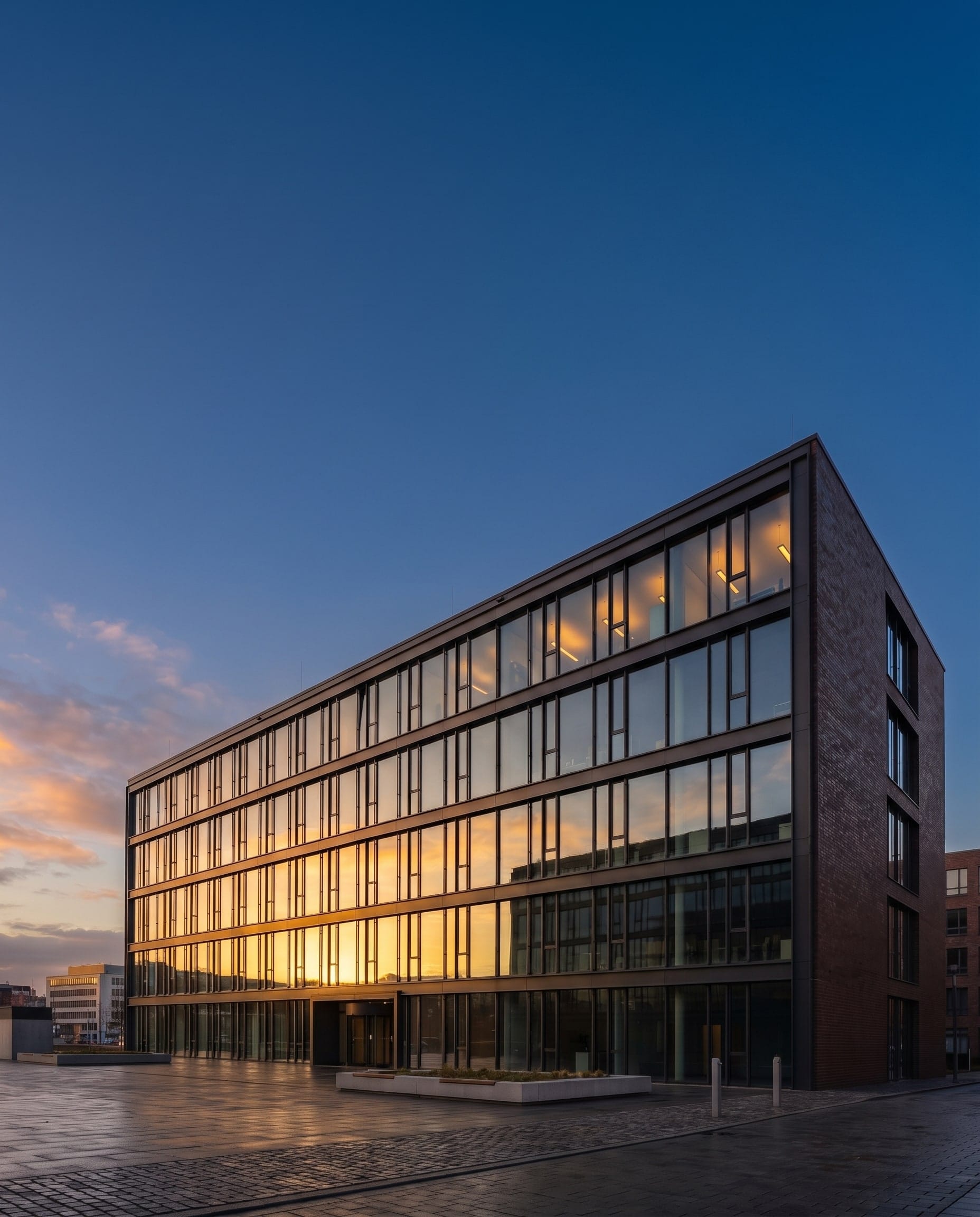 Bürogebäude mit Glasfassade im Abendlicht, davor ein gepflasterter Platz